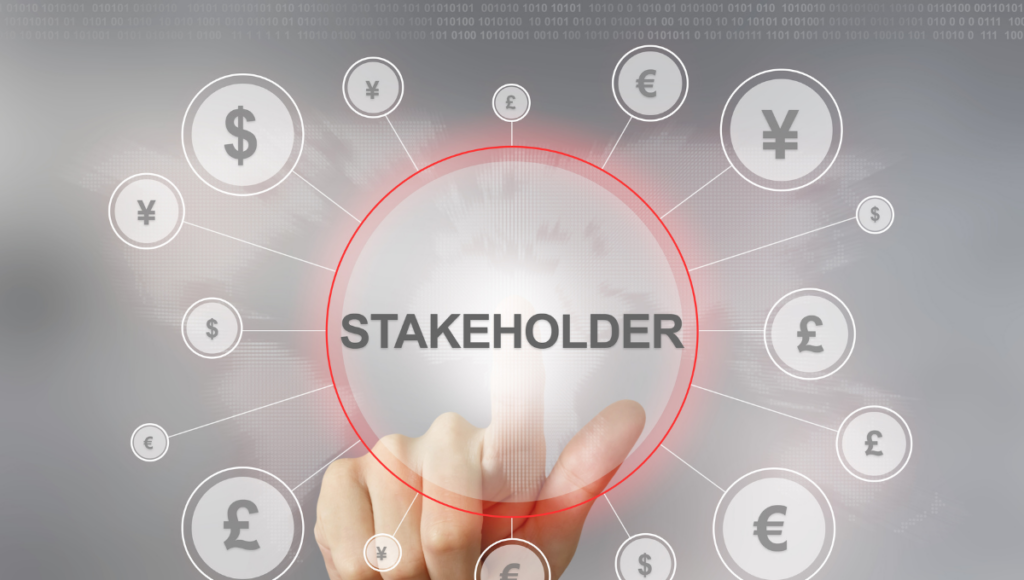 Photo of a hand touching a circle with "Stakeholder" in the center surrounded by foreign currencies.