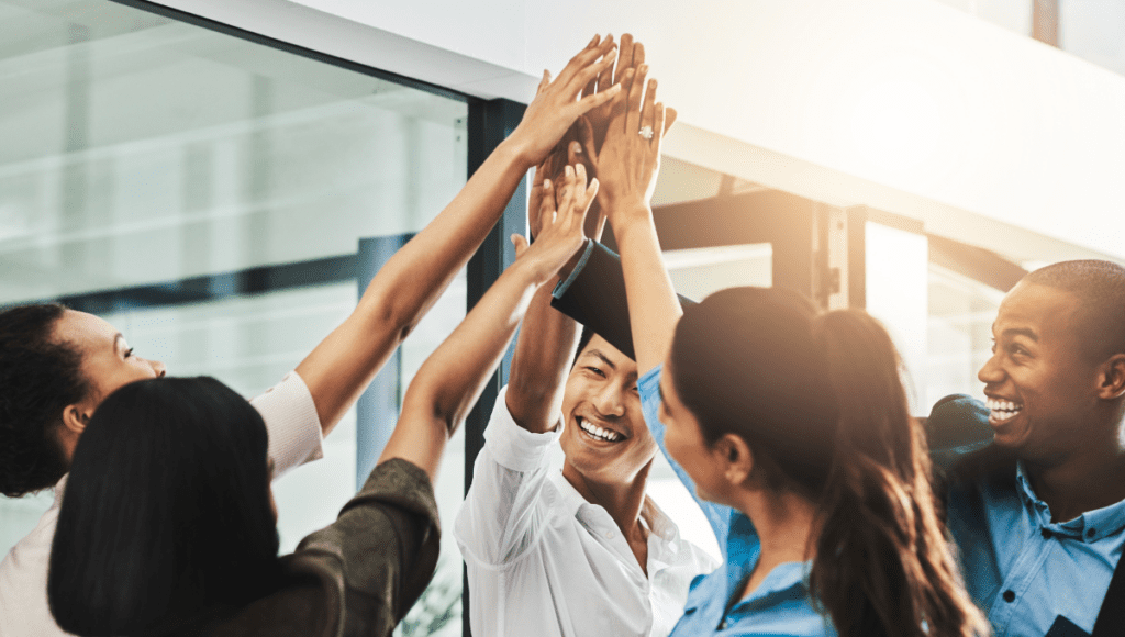 A photo of a team of project managers communicating in harmony, smiling, and high-fiving.